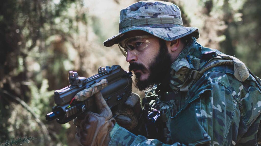 Homem com arma e roupa camuflada, jogando airsoft.
