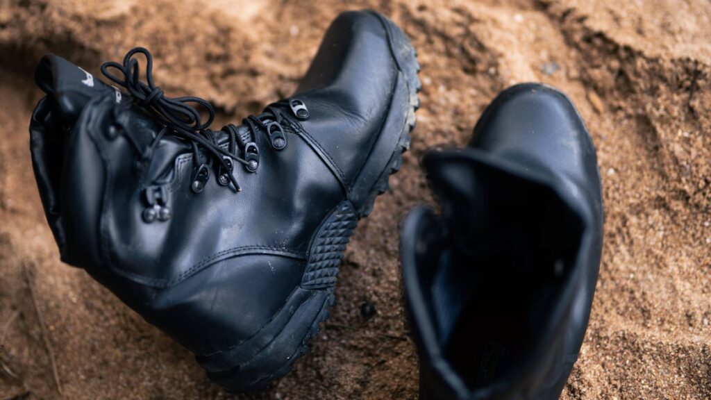 Bota tática preta sobre a areia, com foco no solado e nos detalhes do cadarço reforçado.