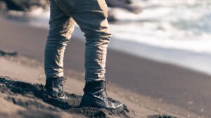Pessoa usando botas Acero em uma praia, com as ondas ao fundo e areia ao redor.
